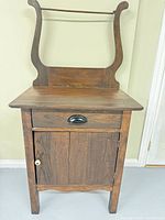 Front view of dark-stained oak washstand showing drawer, cabinet door, backsplash and towel rail