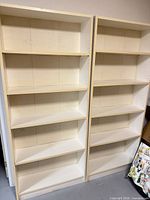 Front view of both off-white Ikea bookshelves showing five shelves each