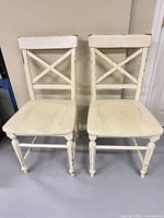 Front view showing both off-white distressed wood dining chairs with X-back and turned legs