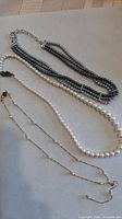 All three necklaces laid out: grey multi-strand, white graduated, gold-tone station