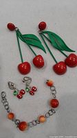 All jewellery pieces grouped: large plastic cherry earrings, small metal cherry earrings, peach bead bracelet