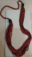 Full view of necklace showing single red bead strand and multi-strand orange/brown seed bead section