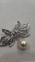 Front view of silver-tone crystal bow brooch with faux pearl drop
