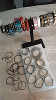T-bar stand holding assorted metal, enamel and plastic bangles plus additional bracelets laid on board
