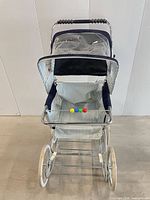 Front view of vintage doll carriage showing metal frame, striped fabric, clear canopy, multicolor beads, wheels