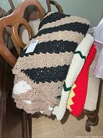 Stack of three crocheted afghans on chair, tan/black/white on top, cream/green middle, red/yellow bottom