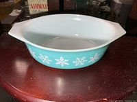 Side view of turquoise Pyrex oval dish showing white snowflake pattern