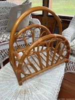 Front angle of rattan magazine rack showing handle, slat base and arched sides