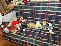 Lineup of all plush toys arranged on plaid sofa, shows both doll stands
