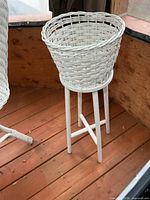 Full view of white wicker planter on wood stand