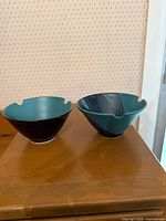 Two teal and black Peter Price bowls side by side on table