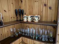 overview of mixed glassware on corner shelves showing steins, black flutes, various clear glasses and shot glasses
