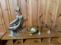 All four brass decor items on shelf: dolphin sculpture, bowl, pair candelabras