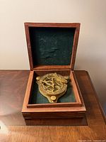 wooden box open displaying brass sundial compass inside