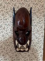 front view of carved horned mask mounted on wall