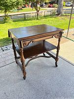 Full view of tea cart showing drop-leaf raised, lower shelf, turned legs, casters