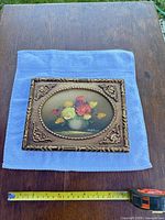 Front view of framed painting on blue cloth with tape measure showing size