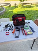 All items arranged on table including tool bag, hammer, pipe wrench, hacksaw, screwdriver, tape, staples
