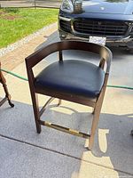 Front view of bar stool showing wood frame, faux leather seat and brass footrest