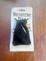 Front view of black suede medicine bag with feather charm on backing card