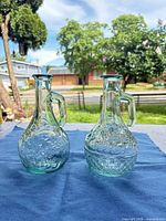 Pair of aqua pressed glass cruets side by side on cloth