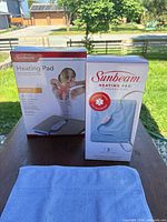 Front view of both Sunbeam heating pad boxes and blue pad cover