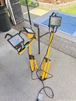 Two yellow tripod work lights with cords and three lamp heads