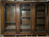 Front view of three-door wooden cupboard showing glass panels and shelves