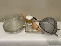 Group shot of all items: stacked pie plates, measuring cup, square dish, nut grinder, rolling pin, strainer