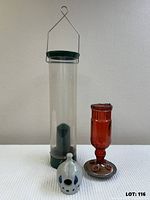 Group view of three items: tube feeder, red hummingbird feeder, clay birdhouse