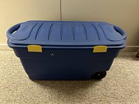 Closed Rubbermaid blue storage box with yellow latches and wheels visible
