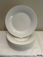 Stack of eleven white dinner plates with one displayed upright