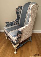 Left front view of the reupholstered wingback chair showing mixed fabric patterns, painted legs and stretcher