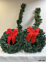 two faux fir wreaths standing, red bows visible