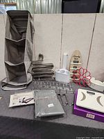 overall view of lot on table including hanging organizer, pant hangers, scale, sign, scarf hanger, caddy, packaged linen, hooks