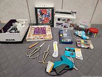 All items laid out including book, shears, glue gun, thread containers, handheld sewing machine box