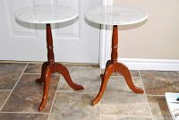 Pair of round wood side tables with white marble tops positioned side by side on tile floor.