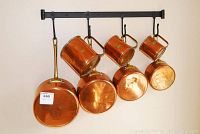 Long-handled copper pot and four D-handled pots on black 22-inch metal rack.