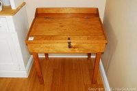 Front view of the antique wooden writer's desk with slanted lift top closed, showing natural wood finish and metal lock.