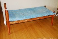 Full side angle of the antique wooden child's bed with blue mattress, showing the bed frame, rope slats, and wooden legs.