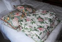 Photo of quilt, two floral throw pillows, and two shams on a bed.