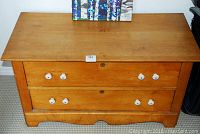 Front view of the wooden dresser showing two drawers with white ceramic knobs and a natural wood finish.