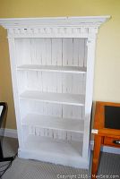 Front view of the 4-tier white wooden bookcase showing its ornate top trim and four shelves.