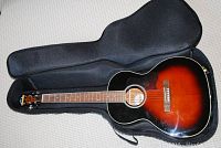 Full view of sunburst acoustic guitar in open black soft shell case on carpet