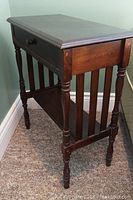 Older solid wood side table with drawer seen from the front corner, showing turned legs, drawer pull, and lower shelf.