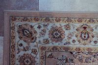 Close-up of corner of one rug showing beige, cream, brown floral border pattern