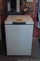 White small chest freezer, top view closed showing minor marks and dent on right side.