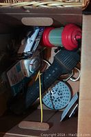 Box containing red and green foot pump, black flashlight, shower head, and other miscellaneous camping and home accessories.