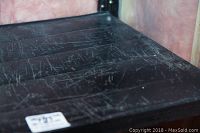 Close-up image of a black metal shelf surface showing numerous scratches and wear marks.