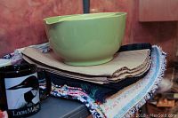 Green mixing bowls stacked on top of several folded kitchen towels and cloths with a black mug visible in the foreground.